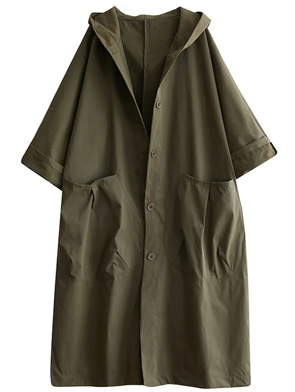Donna cammina in città con trench lungo impermeabile e oversize, cappuccio alzato, look casual.