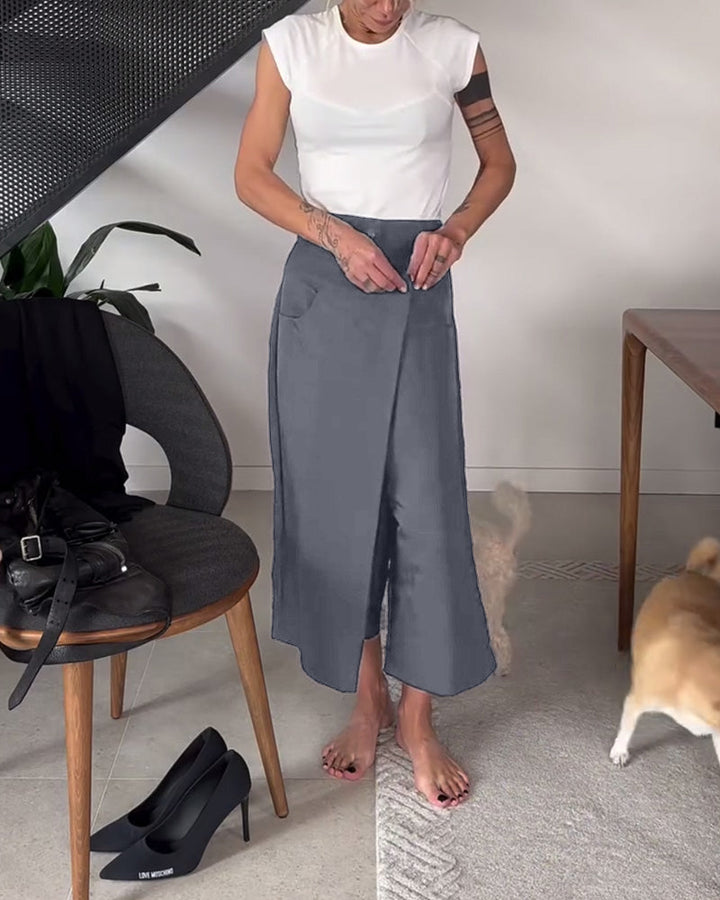Donna indossa pantaloni larghi asimmetrici grigi, abbinati per un outfit moderno ed elegante.