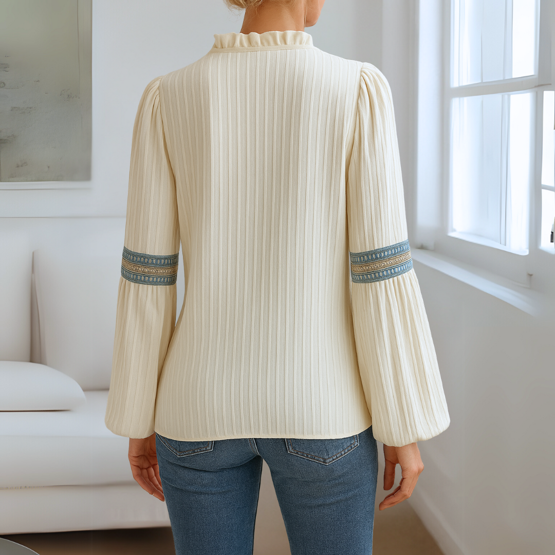 Camicetta femminile color crema con scollo a V profondo, pizzo delicato e volant sulle maniche lunghe.