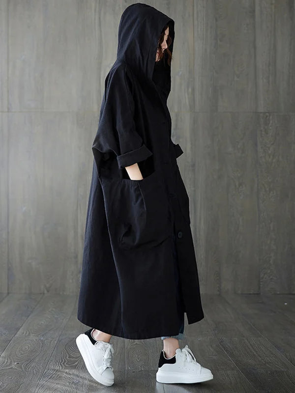 Donna che indossa cappotto lungo impermeabile oversize nero con cappuccio, stile moda urbana.