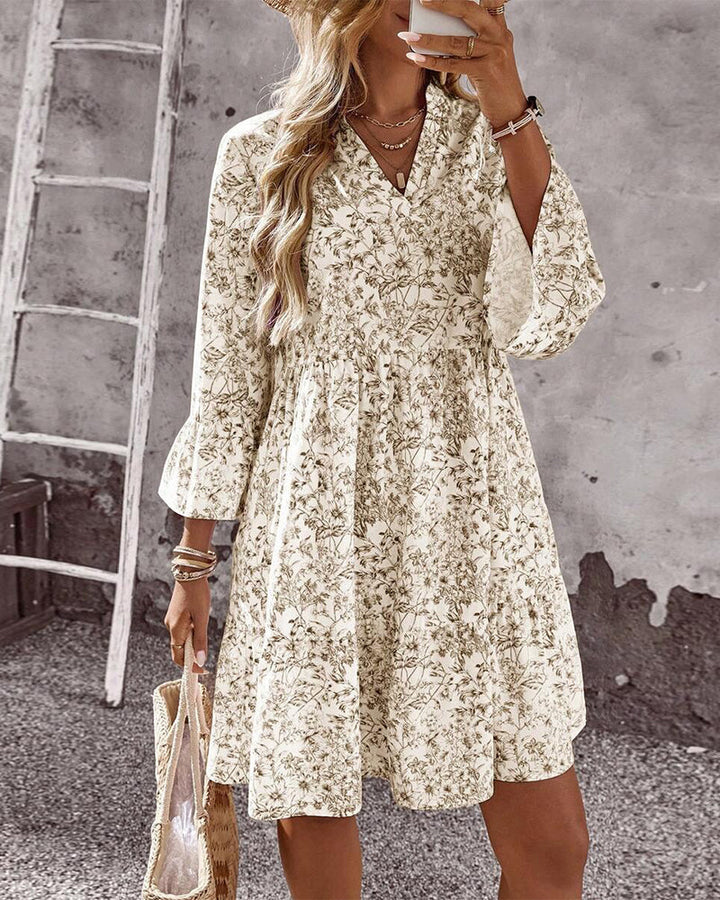 Vestito primaverile beige con collo alto e maniche a volant, decorato da stampa floreale. Moda donna chic.
