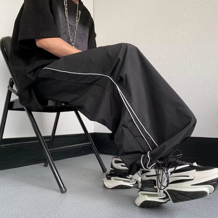 Uomo indossa pantaloni neri streetwear a vestibilità comoda. Ideali per un outfit sportivo e rilassato.