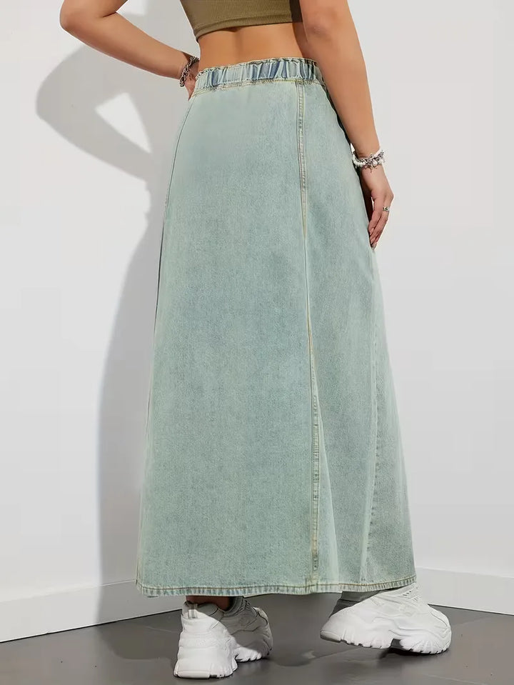 Donna cammina indossando gonna maxi denim blu, vita elasticizzata, stile comodo e casual per il giorno.