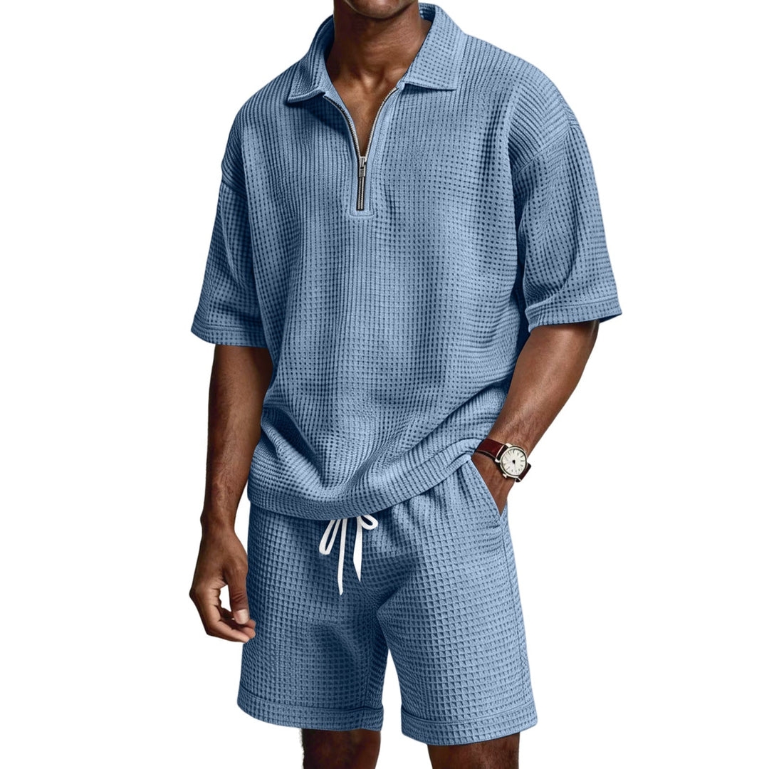 Uomo seduto con completo estivo due pezzi, polo zip e pantaloncini. Ideale per relax estivo.