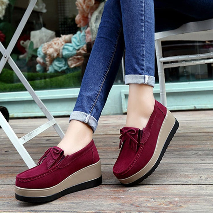 Scarpe donna con zeppa e suola spessa, modello slip-on con fiocco e nappine, look elegante.