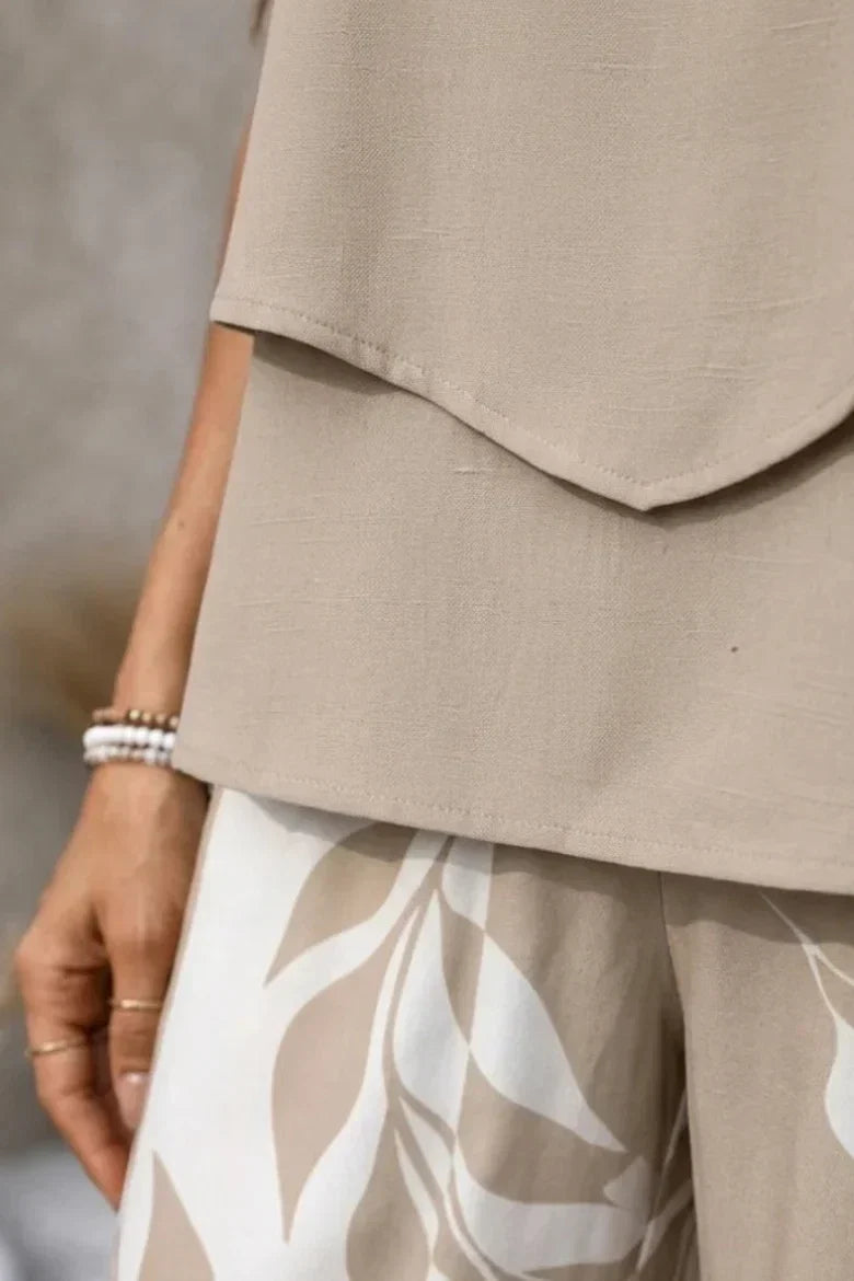 Elegante completo donna beige con top fluido e pantaloni larghi stampati a foglie, perfetto per l'abbigliamento estivo.