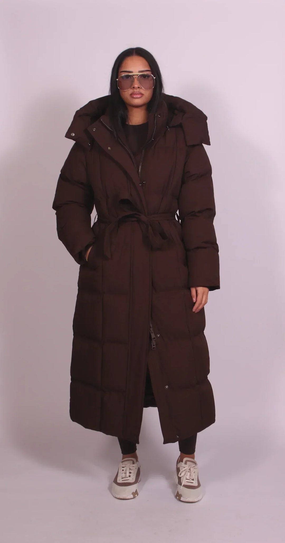 Piumino lungo donna elegante nero, imbottito e caldo, con cappuccio, cintura e collo alto per inverno.