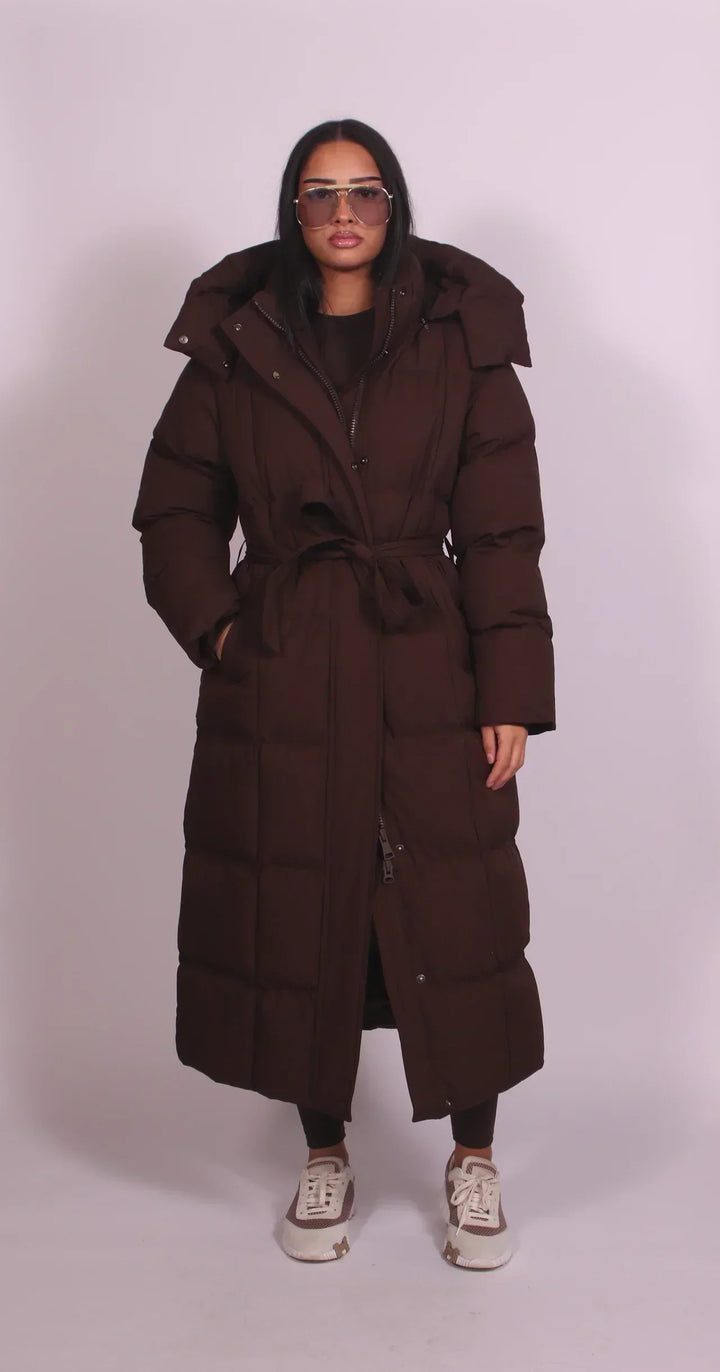 Piumino lungo donna elegante nero, imbottito e caldo, con cappuccio, cintura e collo alto per inverno.