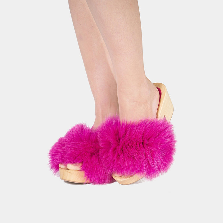 Calzature estive di lusso: zoccoli artigianali da donna con base in legno e morbida pelliccia di volpe fucsia.
