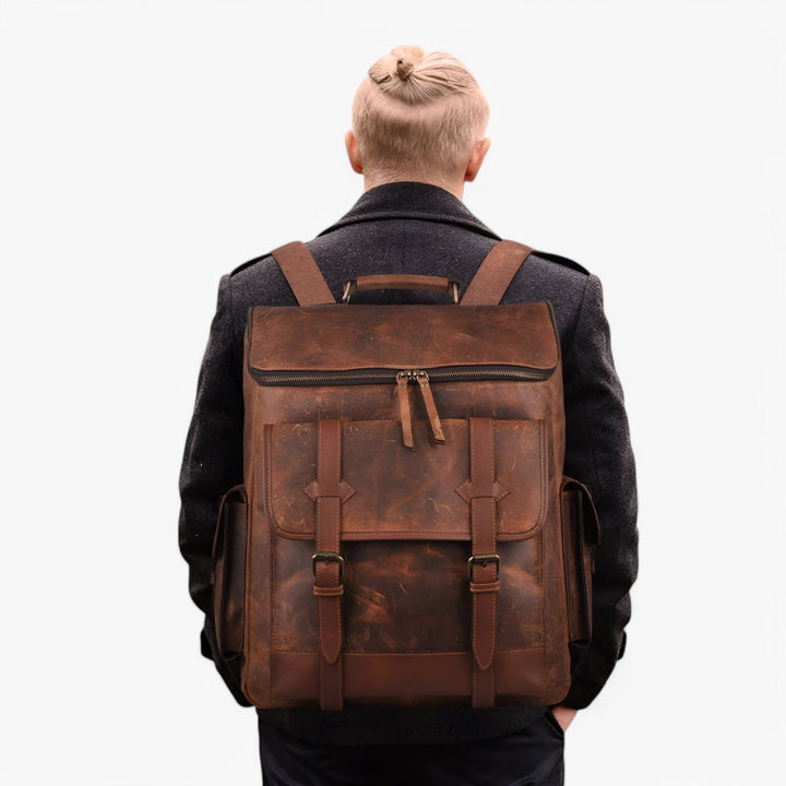 Zaino marrone multitasche da uomo, versatile per viaggio. Dettaglio tasche esterne e capienza.