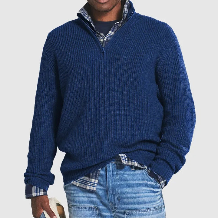 Uomo che indossa un maglione blu scuro collo alto con zip, mostra comfort e stile casual per l'autunno.