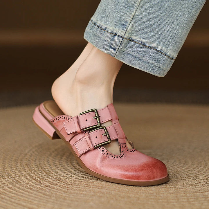 Mules donna in pelle con fibbia metallica e perforazioni brogue, ideali per ufficio o casual.