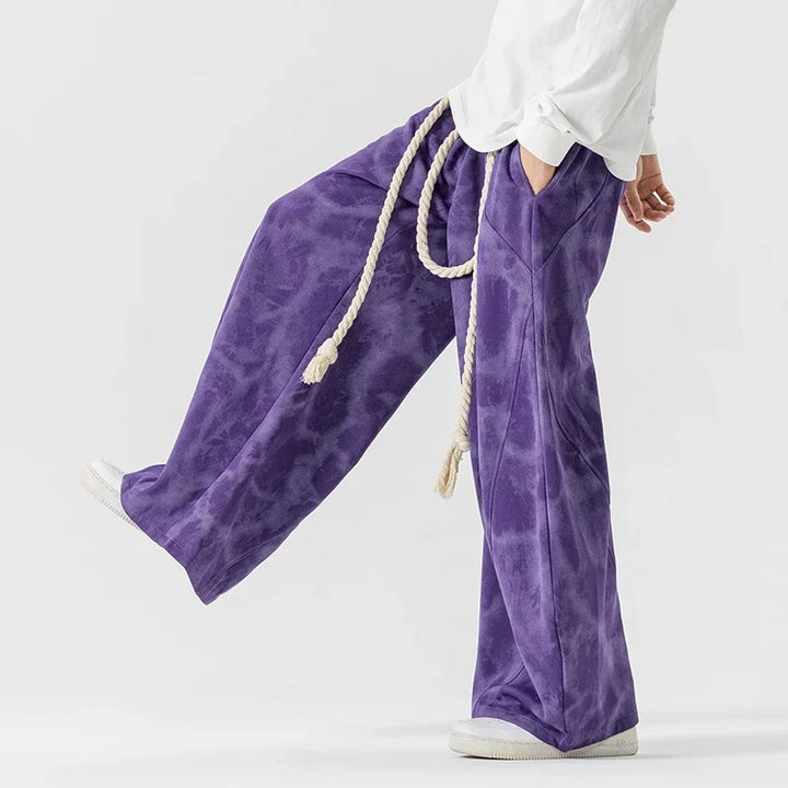 Pantaloni tuta comodi uomo tie-dye, stile gamba larga per moda streetwear. Dettagli in viola, bianco e nero.