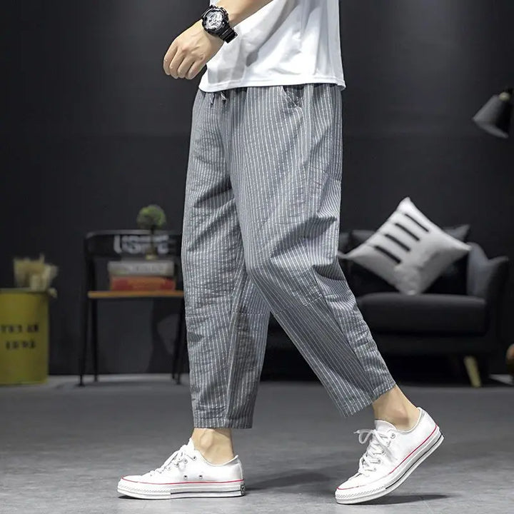 Uomo indossa pantaloni a righe elasticizzati alla caviglia. Ideali per il tempo libero e look casual-eleganti. Vestibilità morbida.
