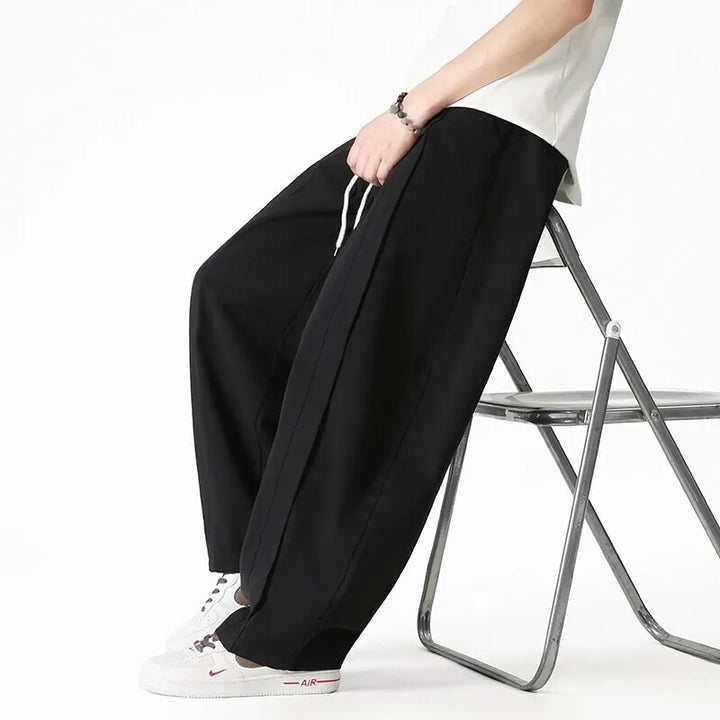 Uomo indossa pantaloni jogging a gamba larga con coulisse, stile casual e comodo per attività quotidiane.