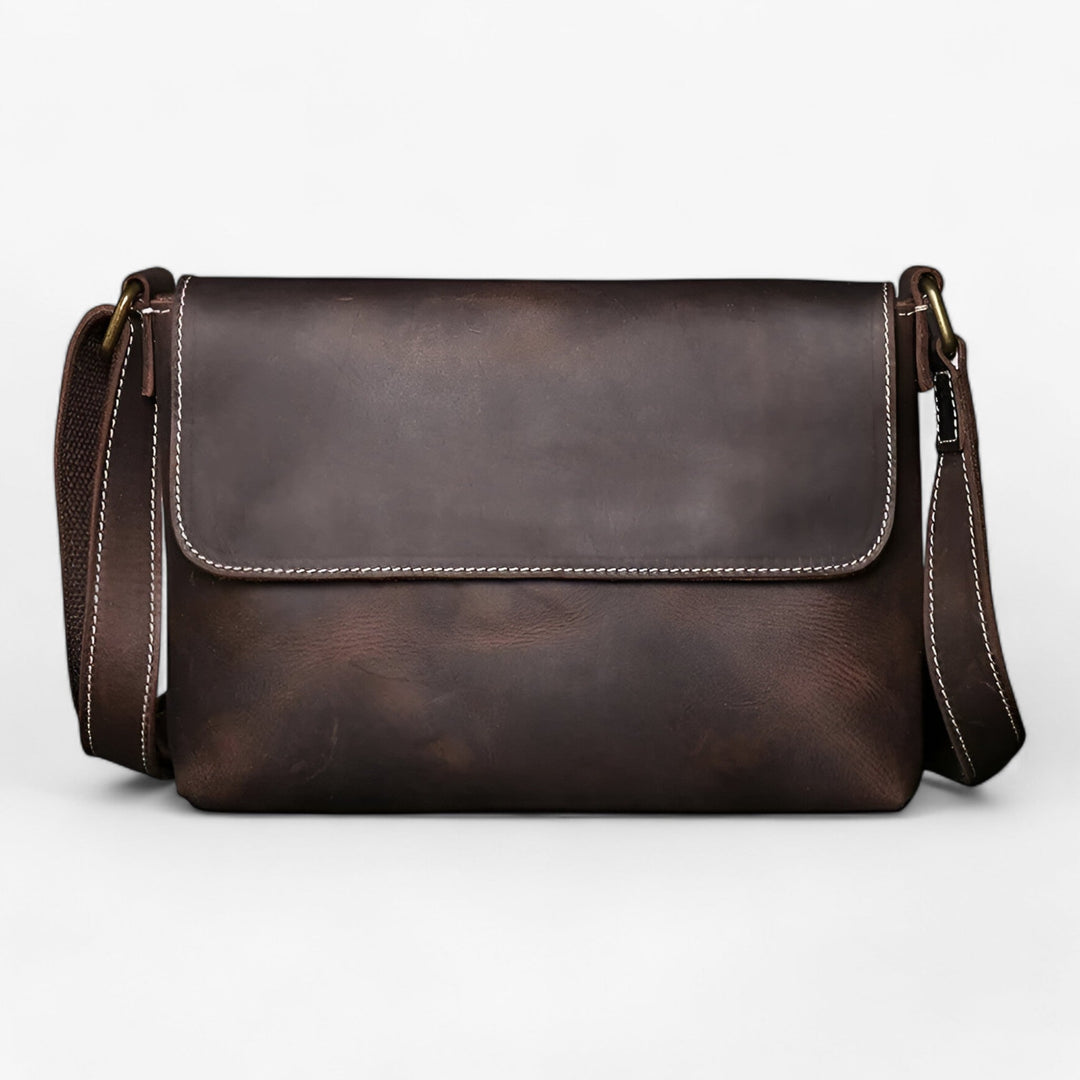 Chiusura con patta e fibbie su borsa messenger unisex, dettaglio della texture del materiale sintetico.