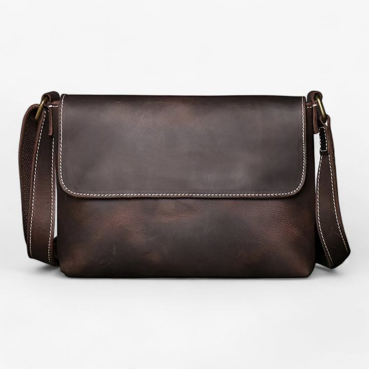 Chiusura con patta e fibbie su borsa messenger unisex, dettaglio della texture del materiale sintetico.