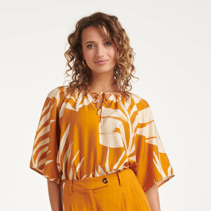 Tunica donna elegante arancio intenso con stampa a foglie. Blusa estiva a maniche corte, perfetta per look casual-chic.