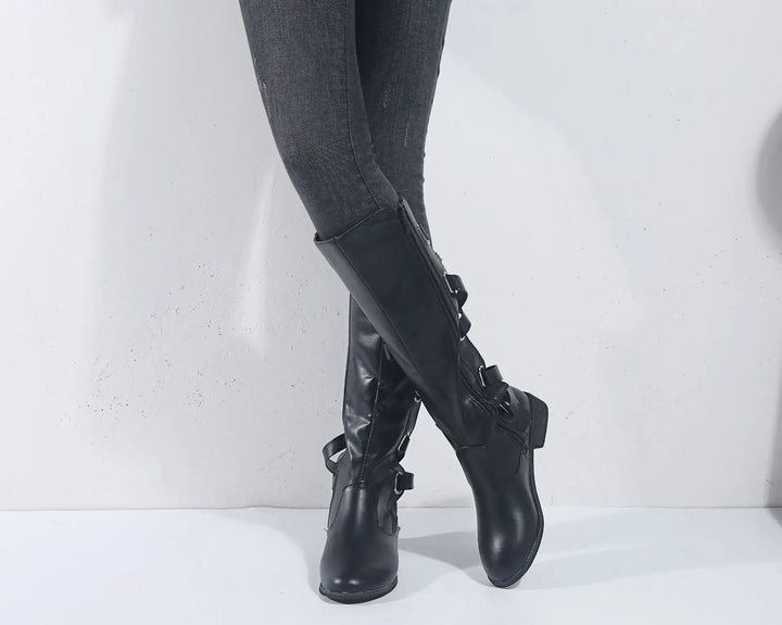 Stivali da equitazione donna al ginocchio in materiale sintetico resistente, con tacco basso e fibbie laterali.