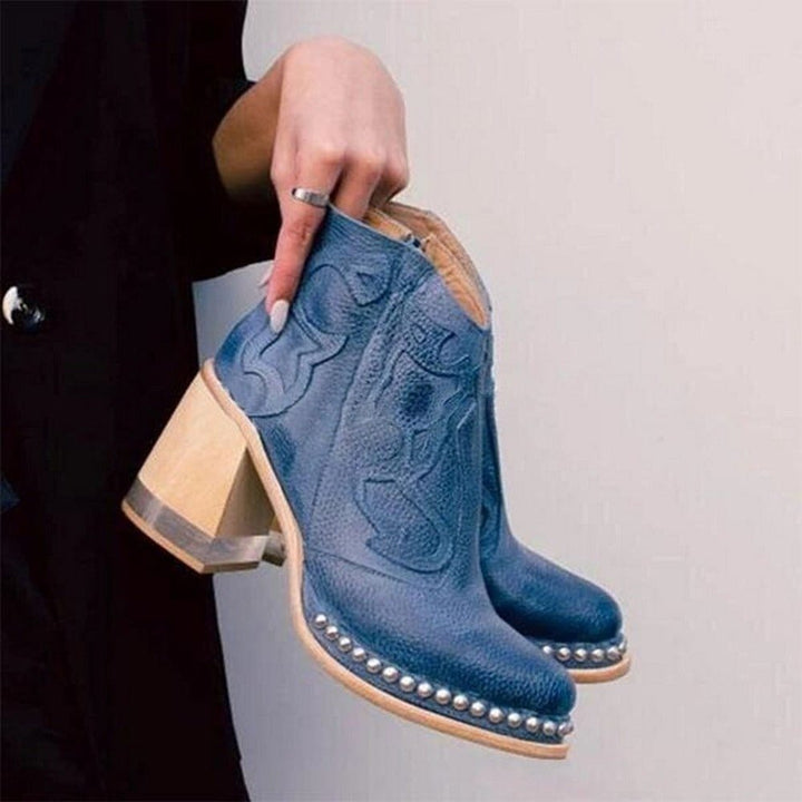 Primo piano di stivaletti cowboy blu da donna in pelle sintetica con ricami, zip e tacco largo.