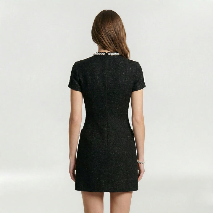Elegante mini abito nero da donna con finte tasche e perle decorative, perfetto per un look da festa o sera.