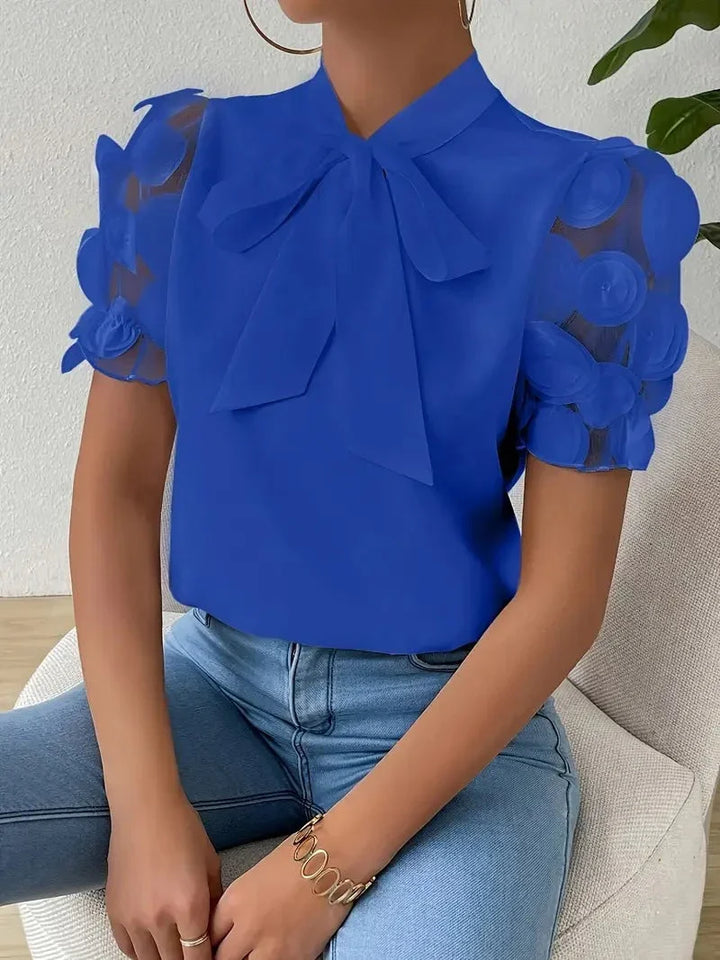 Blusa romantica donna con fiocco, maniche in tulle trasparente e dettagli rose 3D. Ideale per sera e festa.