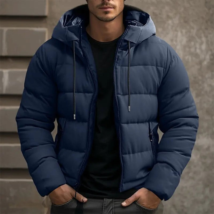 Giacca piumino uomo invernale con cappuccio e tasche zip, calda e trapuntata, disponibile in nero, grigio e blu.