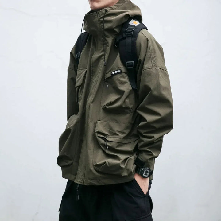 Giacca antivento uomo sportiva con cappuccio, tasche cargo multiuso. Perfetta per attività outdoor e look casual.