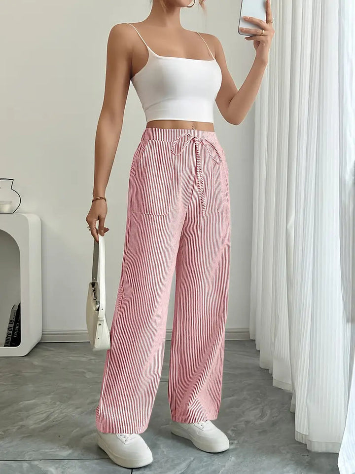 Modella cammina con pantaloni donna a gamba larga a righe, vita alta. Mostra fluidità e comfort. Moda estiva versatile.
