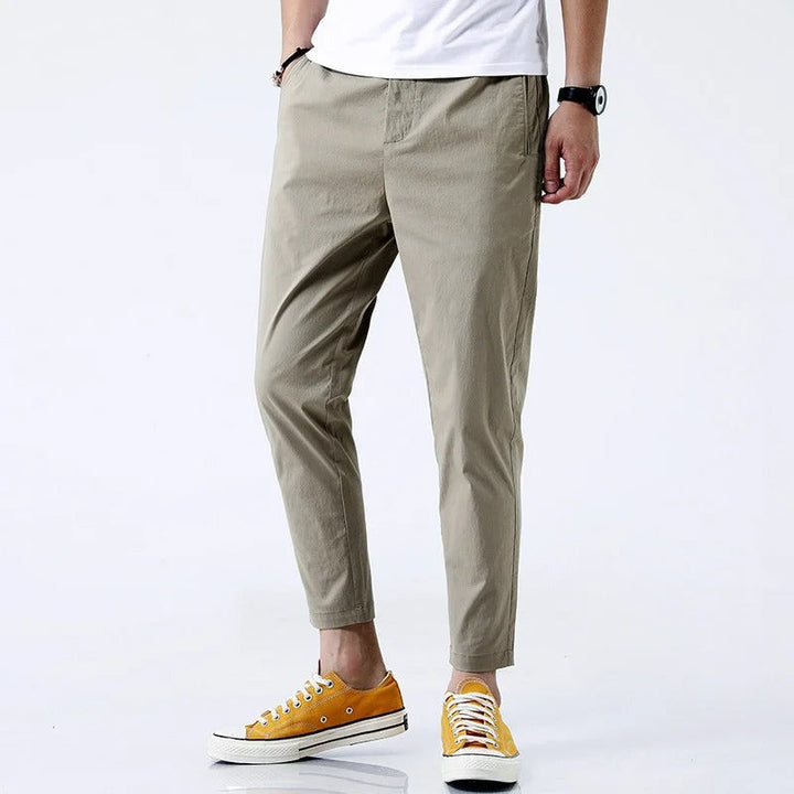 Uomo indossa pantaloni chino straight fit alla caviglia, colore neutro, comfort stretch per eleganza casual e ufficio.