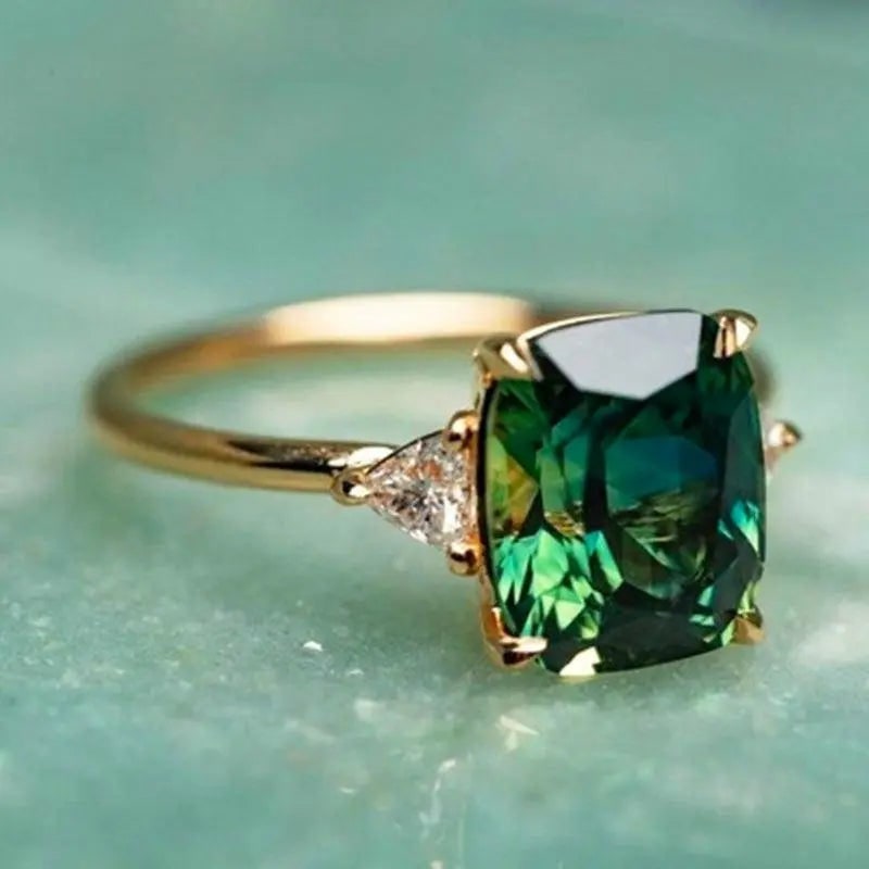 Anello da donna placcato oro con smeraldo centrale taglio cuscino e due diamanti laterali, per fidanzamento o anniversario.
