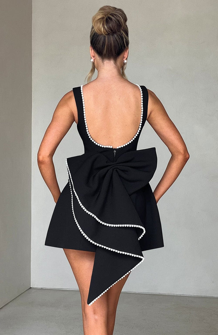 Mini abito nero da festa, scollo a barca e fiocco grande, perfetto per serate eleganti d'autunno.