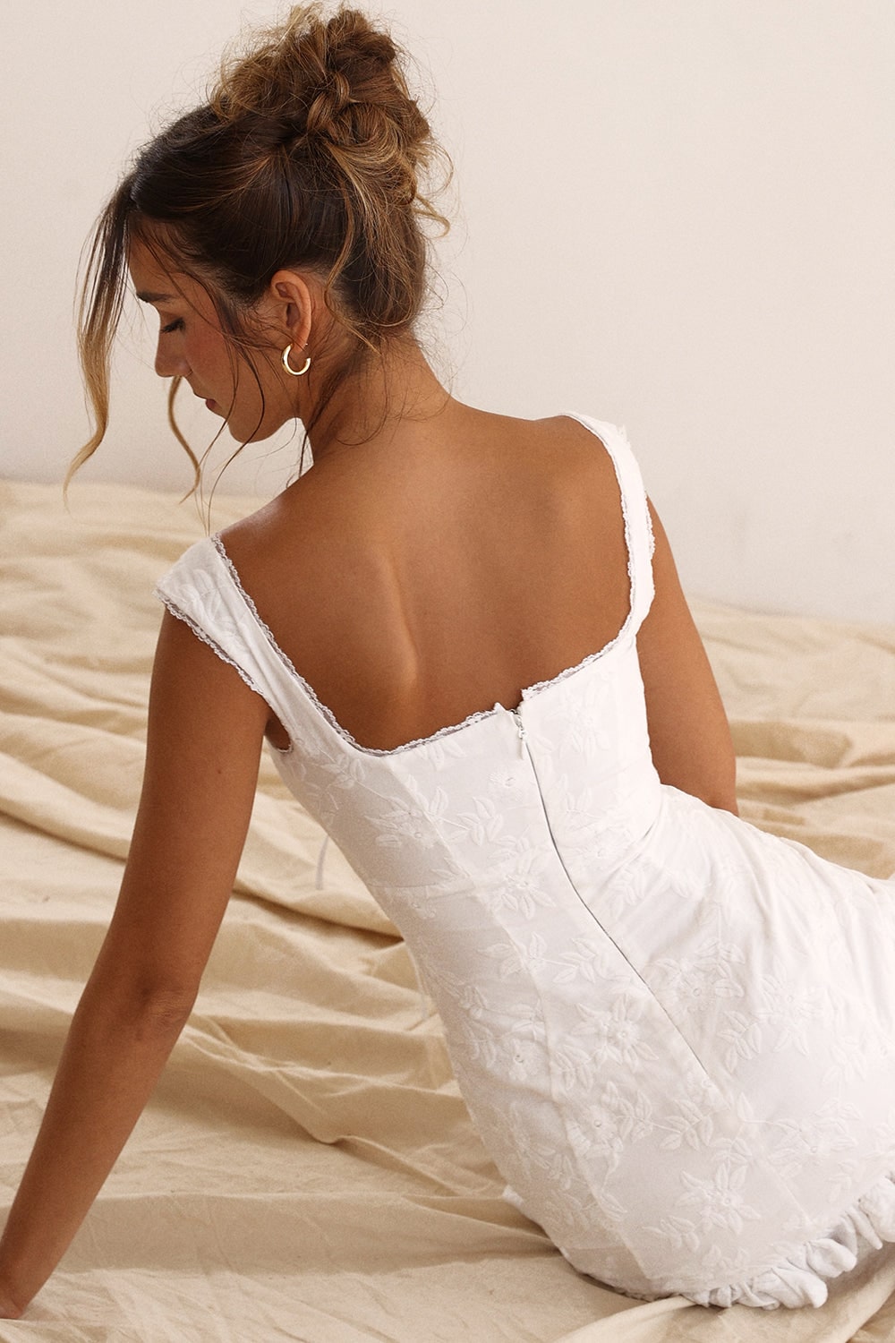 Miniabito estivo bianco per donna, con dettaglio nodo frontale, orlo a balze e taglio corto elegante.