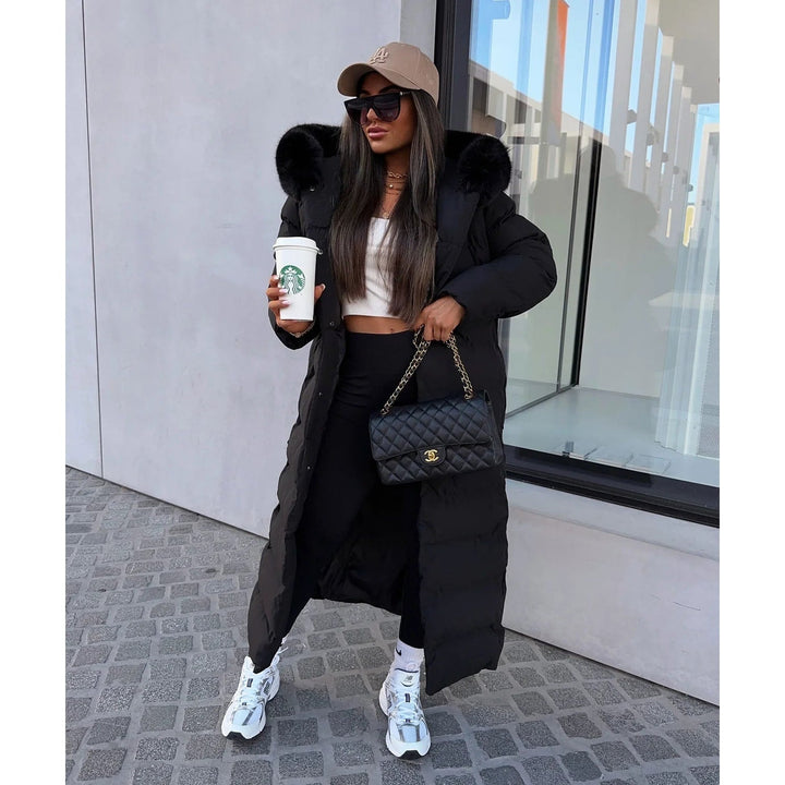 Piumino lungo trapuntato da donna con cappuccio in pelliccia sintetica e cintura, per un inverno chic.