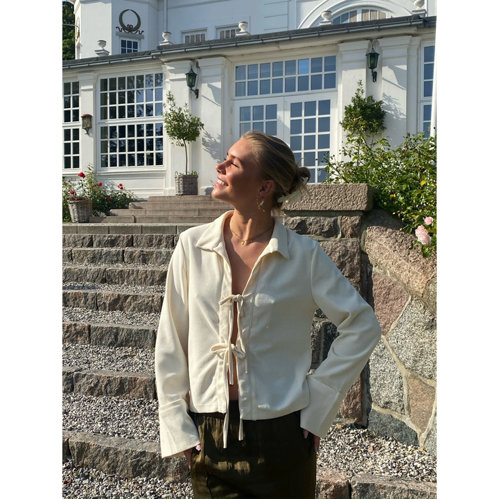 Blusa donna elegante bianco crema con fiocco, maniche lunghe e ampi polsini, perfetta per ufficio e occasioni speciali.