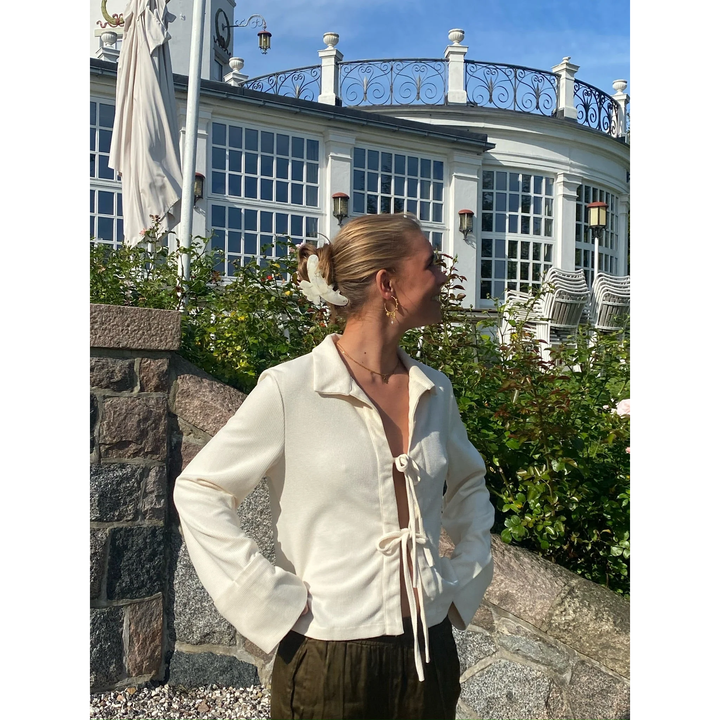 Blusa bianco crema da donna con fiocco frontale e maniche lunghe, dettagli polsini ampi per look raffinato.