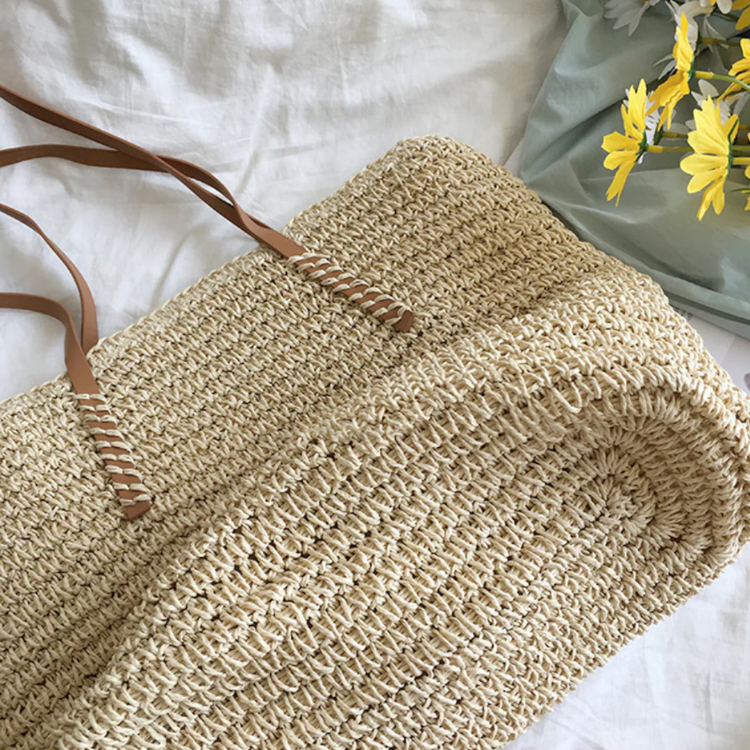 Borsa tote estiva in paglia naturale intrecciata, stile casual elegante, con manici e dettagli in ecopelle marrone.